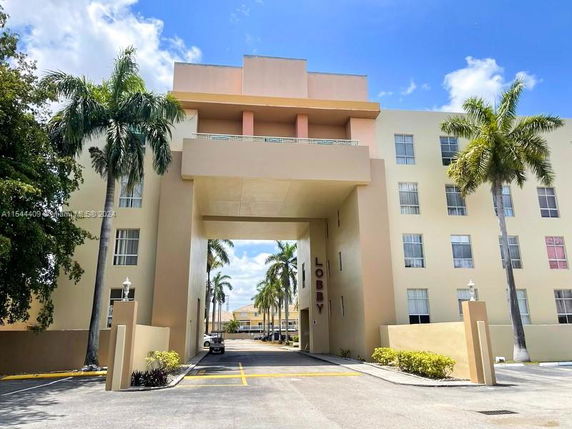 Front view of a multi-story building with a large entrance archway and palm trees.
