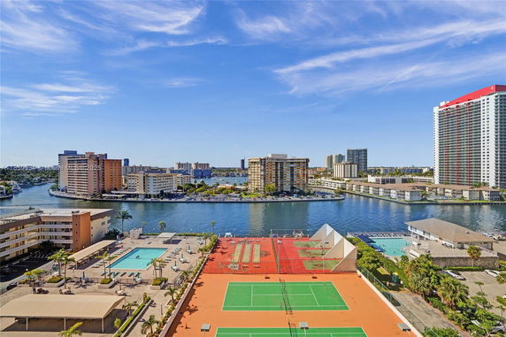Panoramic view of high-rise buildings near a waterway with nearby swimming pools and tennis courts.