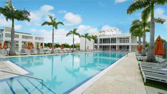 Outdoor swimming pool area with surrounding palm trees and lounge chairs next to a modern building.
