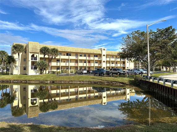 Front view of a multi-story residential building with balconies and a pond in front.