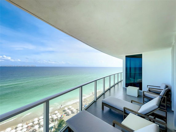 Balcony view overlooking the ocean with lounge chairs.