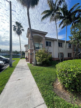 Front view of a two-story residential building with balconies and palm trees.