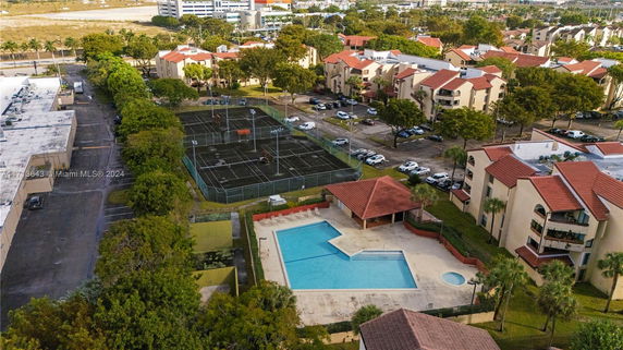 Aerial view of residential area with tennis courts, a swimming pool, and red-roofed buildings.