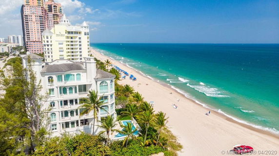 Aerial view of beachfront buildings next to a sandy beach and blue ocean.