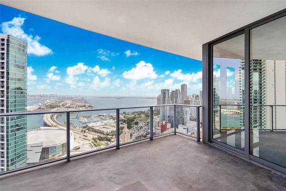 View from a spacious balcony overlooking a cityscape with high-rise buildings and a harbor in the distance.