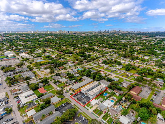 Aerial panoramic view of a suburban area with numerous houses and buildings, with a city skyline in the distance.