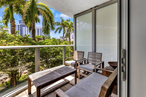 Balcony view with outdoor seating and palm trees in the background.