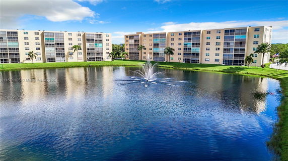 View of multi-story residential buildings with a lake and water fountain in the foreground.
