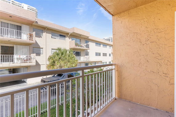 View from a balcony towards an adjacent apartment building with exterior railing and a small portion of the street visible.