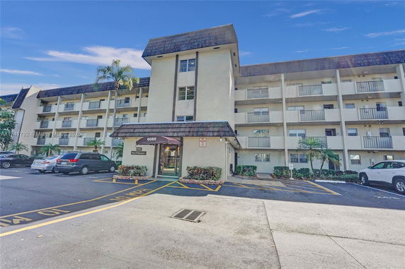Front view of a multi-story apartment building with balconies and a parking area in front.