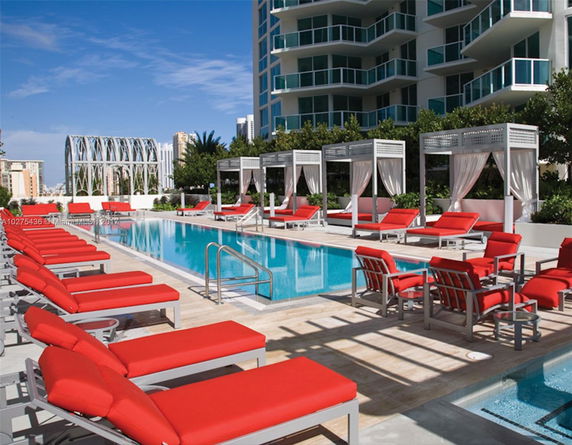 Outdoor swimming pool area with red lounge chairs and cabanas.