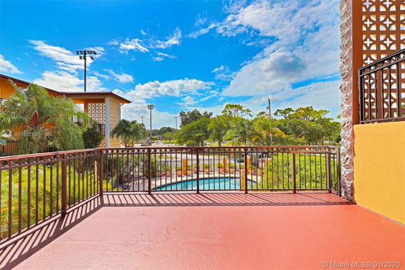 View from a balcony overlooking a swimming pool and surrounding greenery.