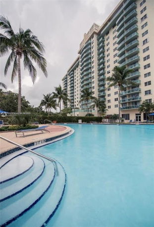 Front view of a multi-story residential building with balconies and a swimming pool in the foreground.