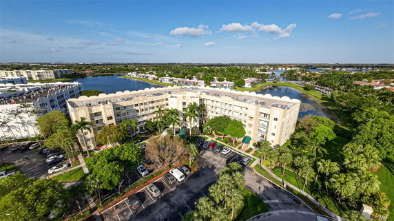 Aerial view of an apartment complex with a lake and lush greenery in the surroundings.