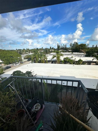 View from a balcony showing rooftops and trees under a blue sky with clouds.