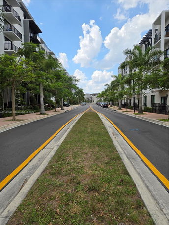 Street view flanked by modern apartment buildings with balconies and trees lining the sidewalk.