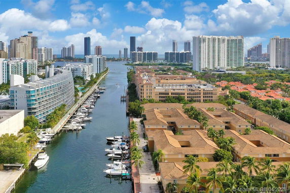 Panoramic view of a cityscape with waterfront, high-rise buildings, and boats docked along a canal.