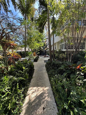 View of a building with lush greenery and a pathway surrounded by plants and trees.