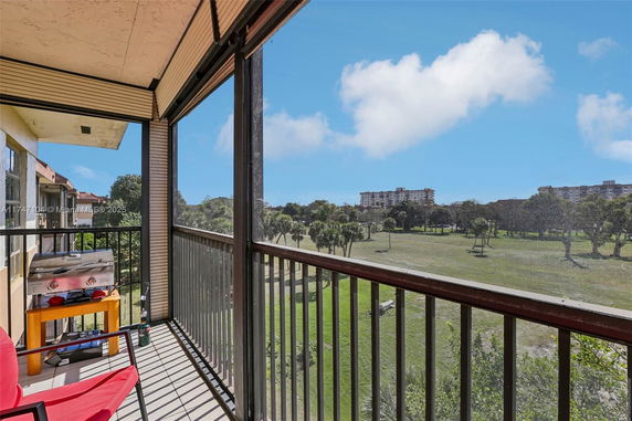 Balcony view overlooking a grassy area and trees with buildings in the background.