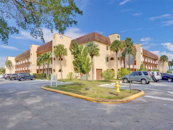 Front view of a multi-story residential building with a parking area and palm trees.