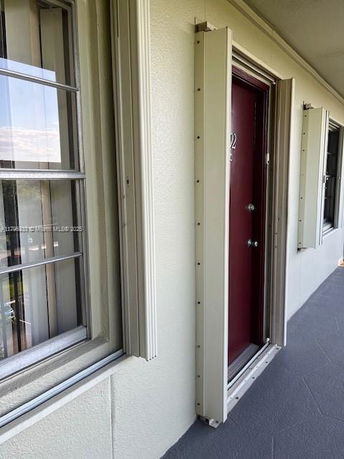 Exterior view of a building hallway with a red door and windows with storm shutters.