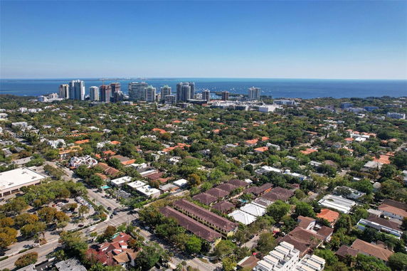 Panoramic aerial view of a cityscape with buildings, greenery, and ocean in the background.