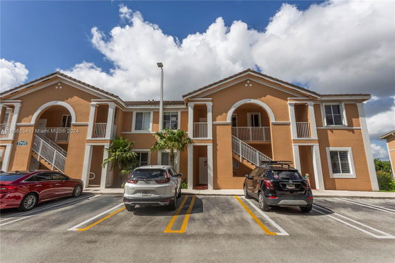 Front view of a two-story residential building with arched entrances and a parking area.