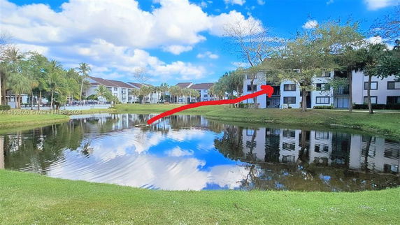 A view of multiple residential buildings surrounding a small pond, with a clear blue sky above.