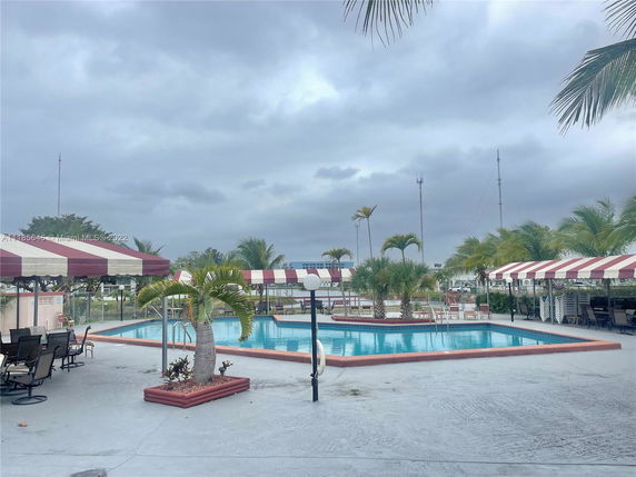 Outdoor swimming pool area with lounge chairs and palm trees.