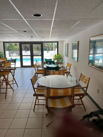 Indoor seating area with glass tables and chairs, adjacent to a large window overlooking a swimming pool.