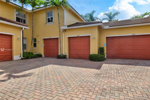 Front view of a townhouse with multiple attached garages, featuring a yellow facade and red garage doors.