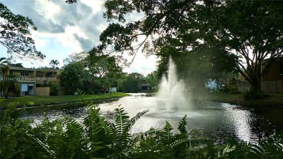 View of a landscaped area with a water fountain and trees.