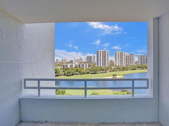 Panoramic view of high-rise buildings and a golf course with a lake, seen from a balcony.