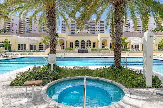 Outdoor view of a pool area with a jacuzzi and lounge chairs, surrounded by palm trees.
