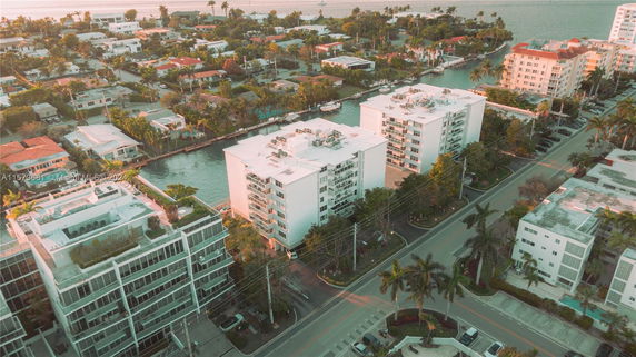 Aerial view of multiple residential buildings near a waterway, surrounded by greenery and roads.