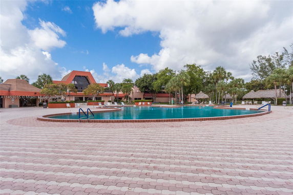 Outdoor swimming pool area with surrounding buildings and palm trees.