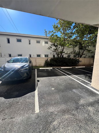 Outdoor parking area with a parked car and a view of apartment buildings.