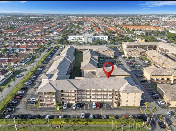 Aerial view of a residential complex with multiple buildings and parking areas, surrounded by a neighborhood.