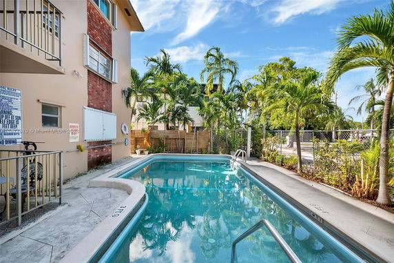 Outdoor swimming pool area adjacent to a building with surrounding tropical plants.