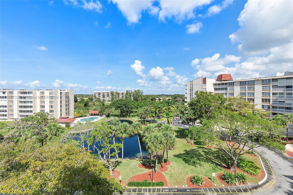 View of multiple residential buildings surrounded by greenery and a pond.