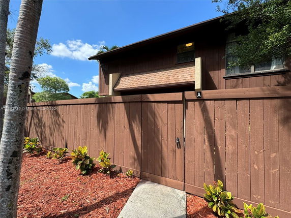 Front view of a two-story brown house with a wooden fence.
