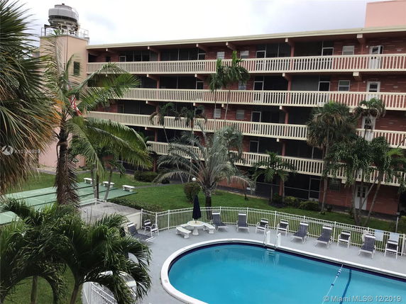 Front view of a multi-story apartment building with balconies and a swimming pool in the foreground.