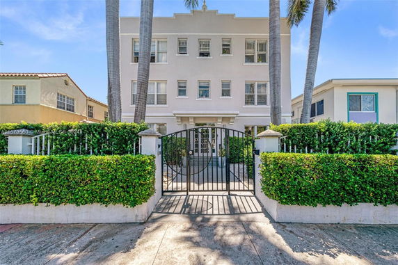 Front view of a three-story apartment building with gated entrance and palm trees.