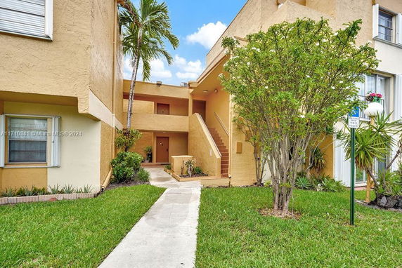 Front view of a multi-story apartment building with tan stucco exterior and stairs leading to the entrance.