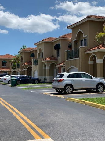 Outdoor parking area with cars parked near a row of two-story houses.