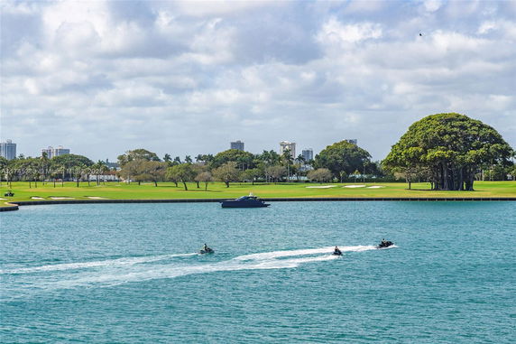 View of a water body with jet skis and a distant shoreline featuring trees and buildings.