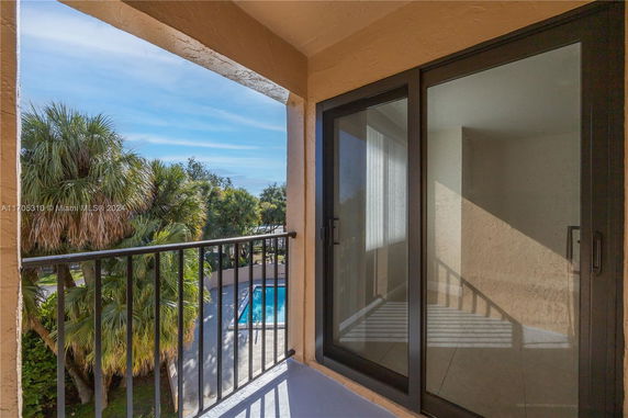 Balcony view with sliding glass door overlooking trees and a swimming pool.