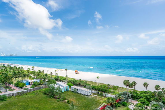 Panoramic view of a beach and ocean with some greenery and structures visible near the shoreline.