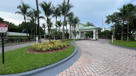 Front view of a gated entry with a small guardhouse and tropical landscaping.