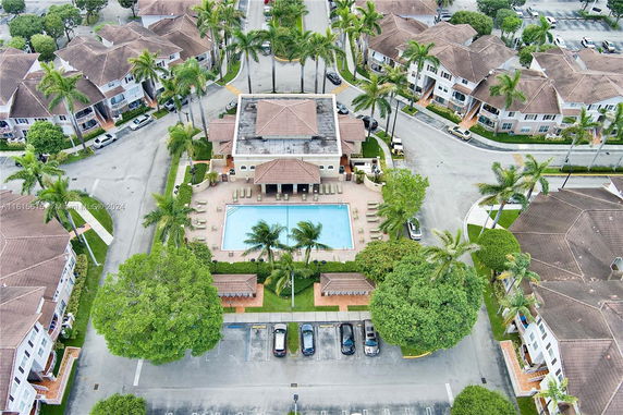Aerial view of a residential complex with a central swimming pool surrounded by buildings and palm trees.